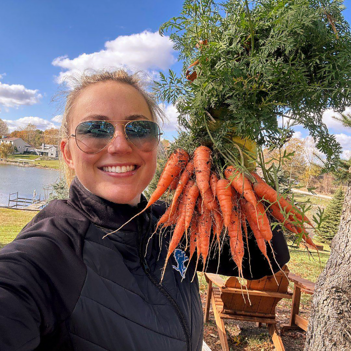 Person holding a bundle of carrots outdoors with a scenic background