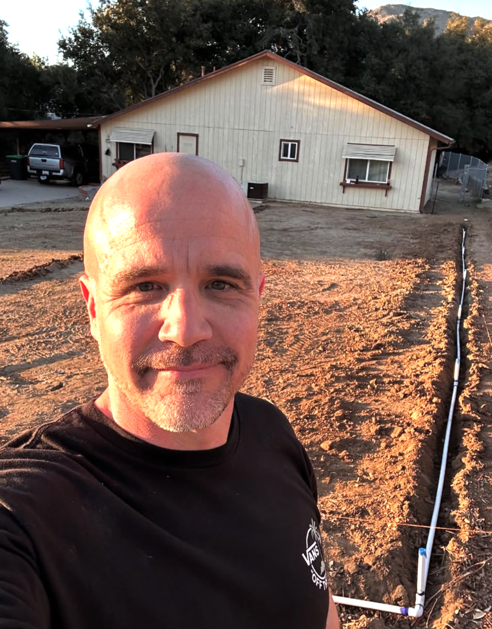 Man standing in front of a white building with trees in the background