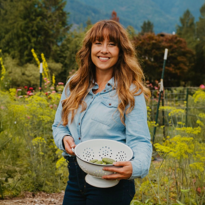 Melissa K Norris holding a colander with vegetables in a garden setting