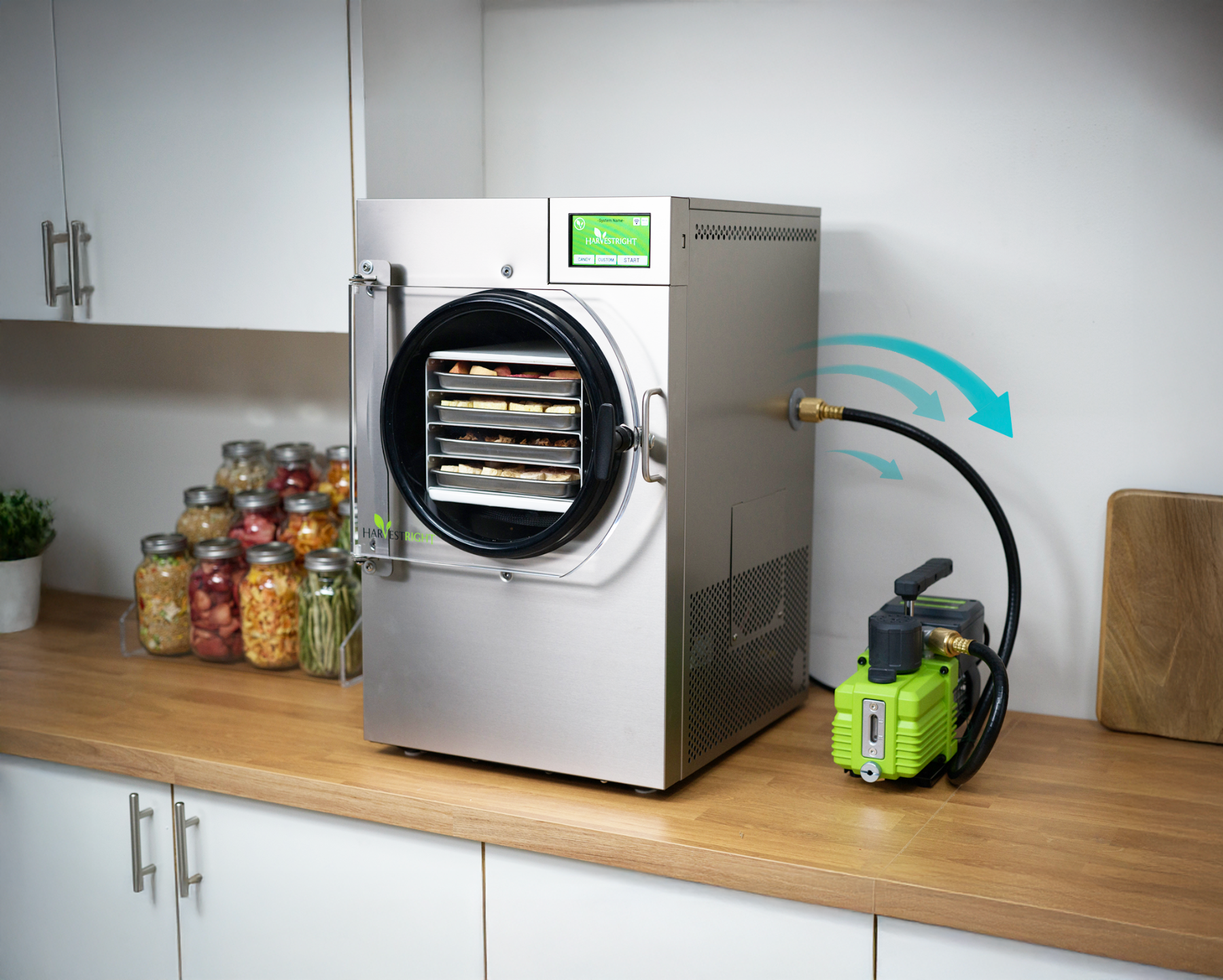 Commercial freeze dryer on a kitchen counter with a pump and jars of food.