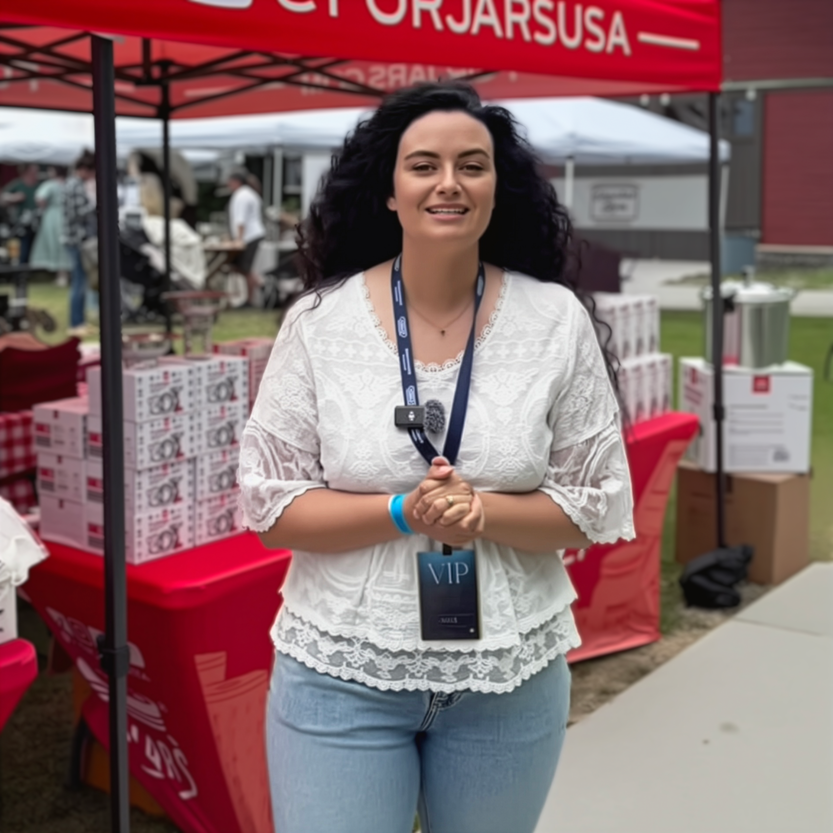 Woman with a 'VIP' badge standing under a red tent at an outdoor event.
