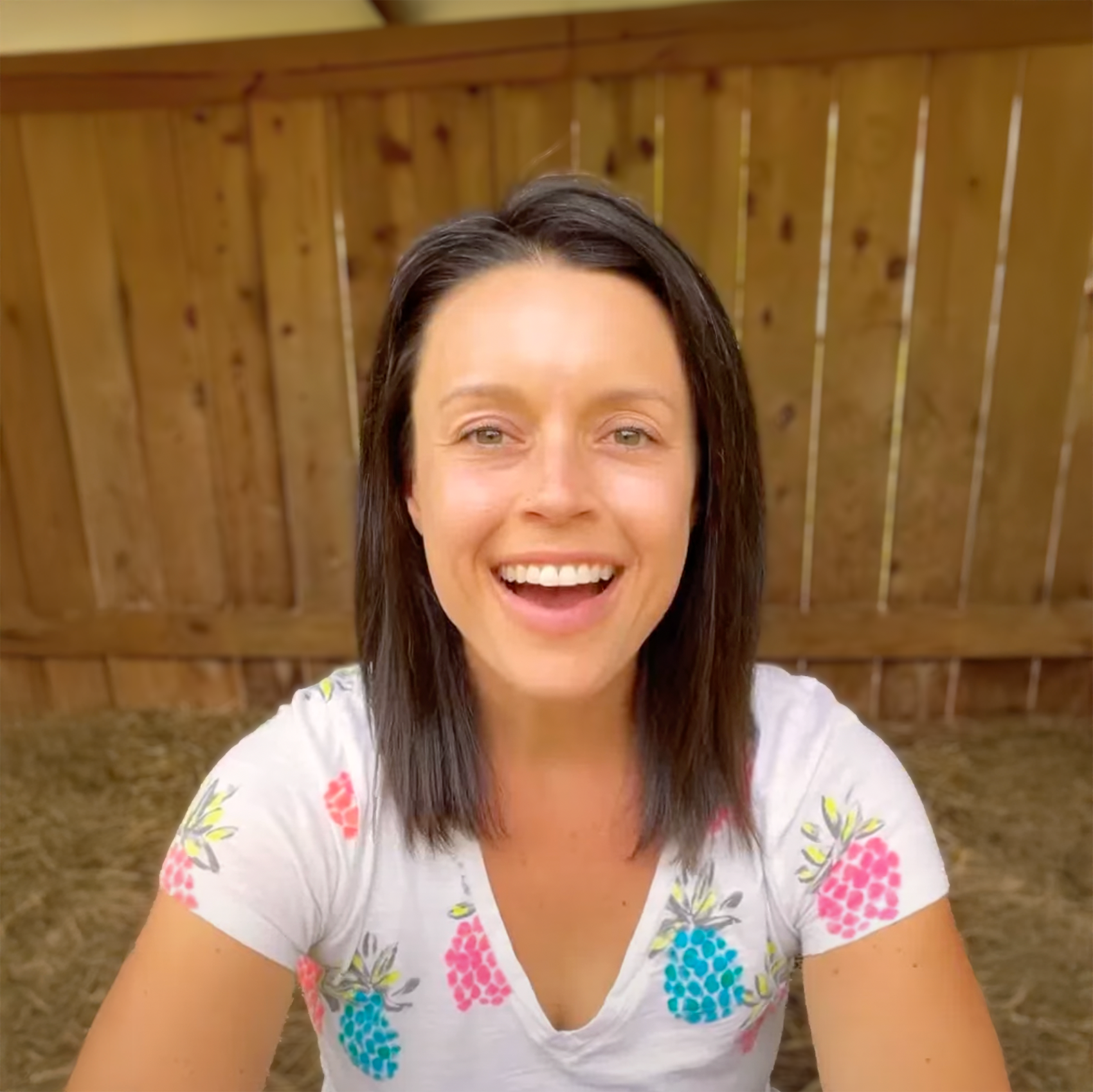 Sara on the farm wearing a white shirt with colorful floral patterns in front of a wooden fence.