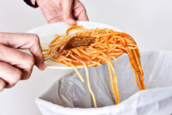 spaghetti being scraped into a garbage can 