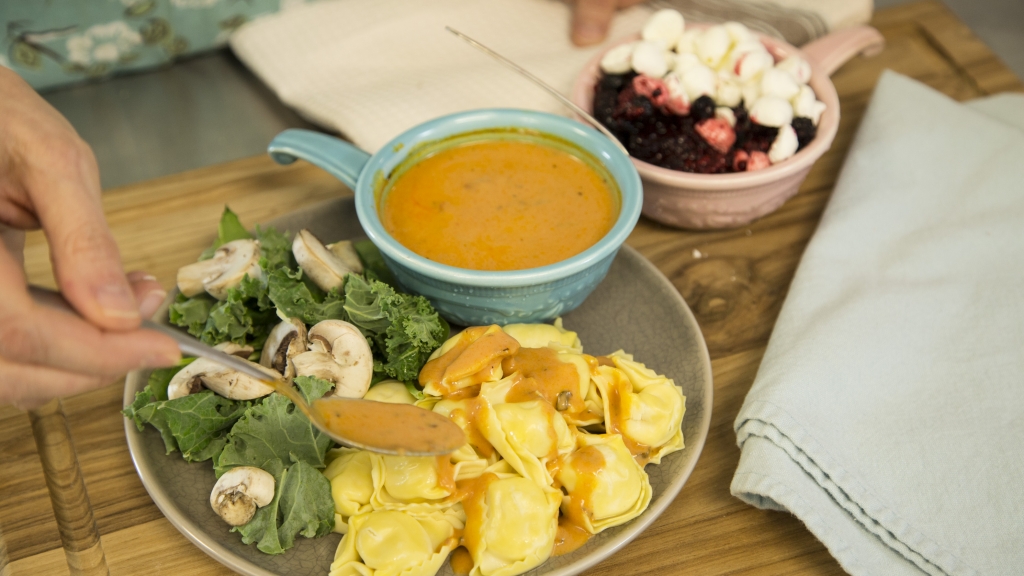 a plate of food with kale, mushrooms, tortellini, and sauce