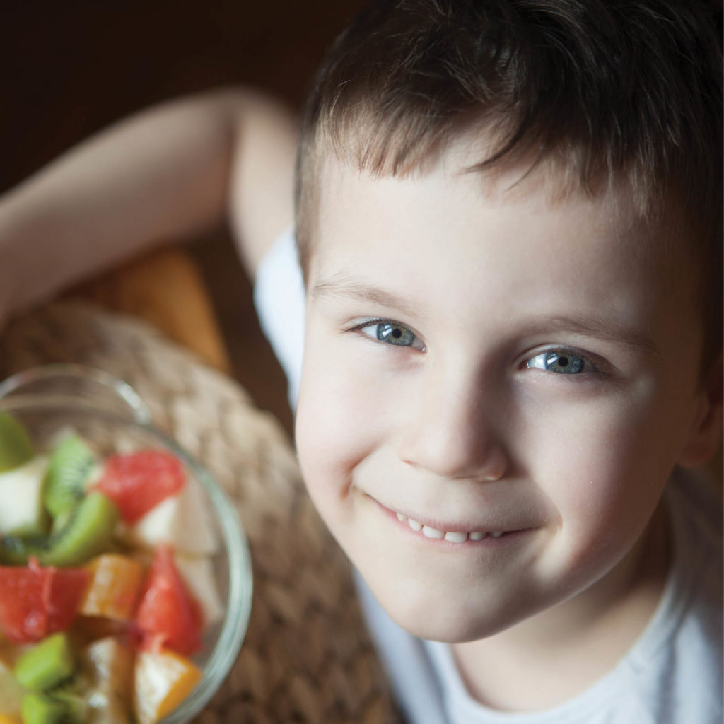 a smiling child with a bowl of fruit