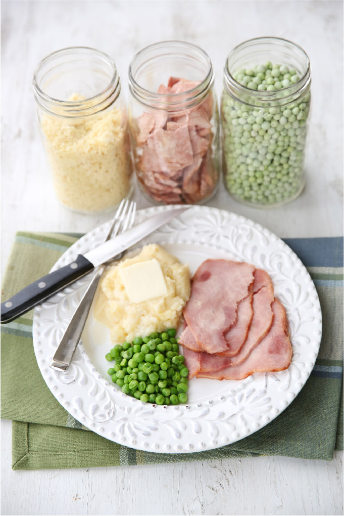 Jars of freeze dried potatoes, ham, and peas. Below the jars: a plate of the same food rehydrated and ready to eat.