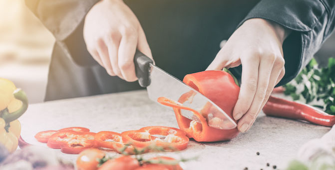 A person chopping a red bell pepper